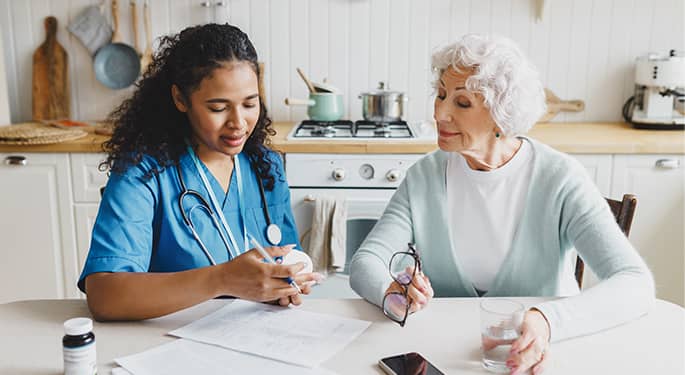 Nurse reviewing medication with an elderly woman at the kitchen table