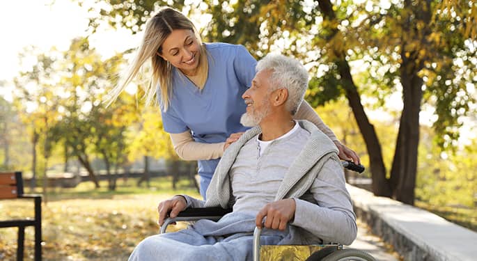 Nurse pushing an elderly man in a wheelchair through a park in autumn