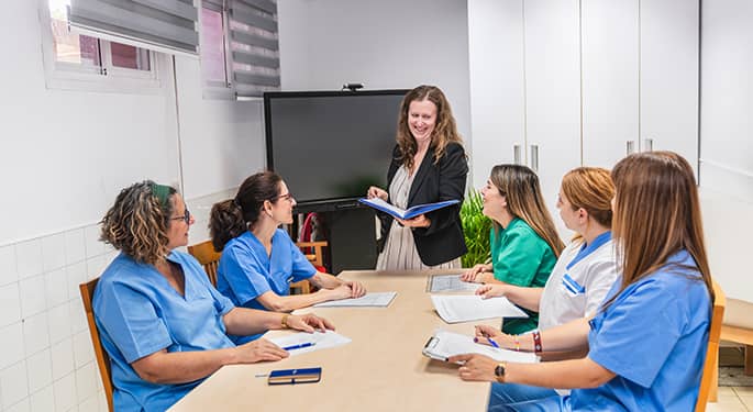 Faded background photo of a presenter addressing a team of caregivers at a meeting