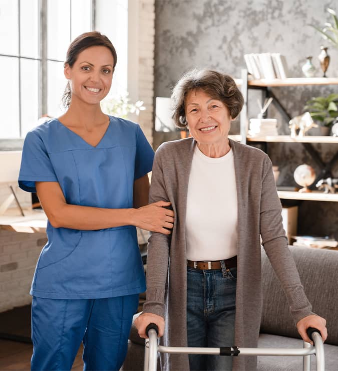 Smiling nurse standing with an elderly woman using a walker at home
