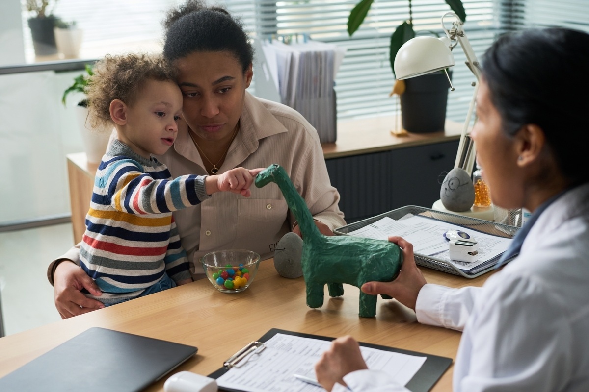 Child during a play-based evaluation for early signs of autism with mother and pediatrician